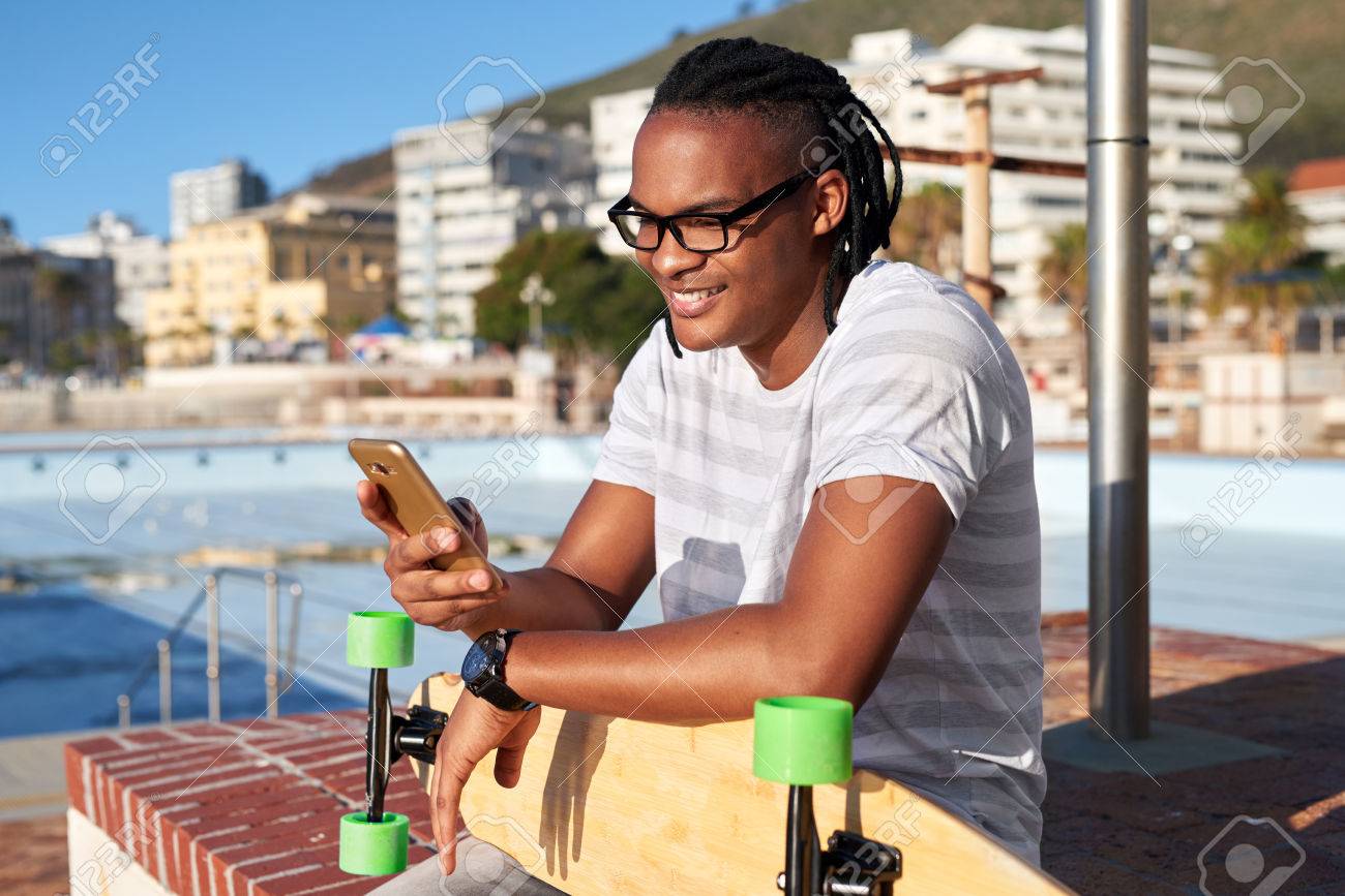 Man with longboard smiling and texting on mobile cell phone, sunny summer day - 84882338 Man with longboard smiling and texting on mobile cell phone, sunny summer day - 84882338
