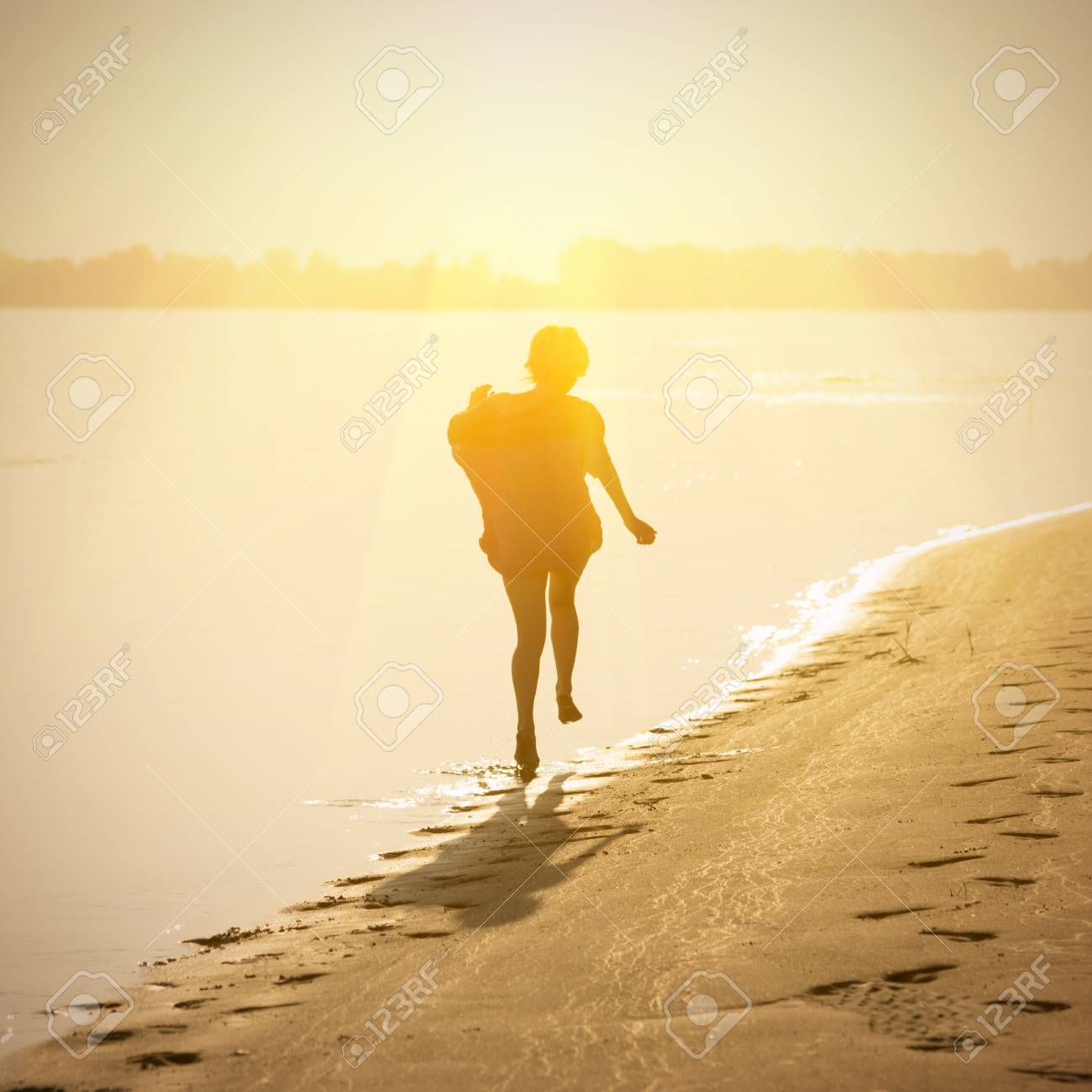 happy blond girl teenager running along the surf line at sunset