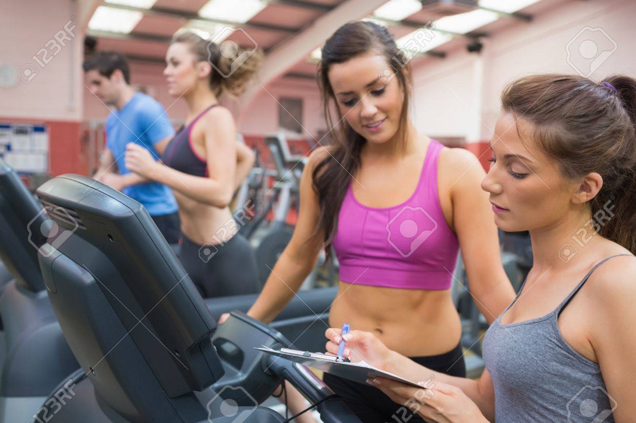 female gym instructor and smiling woman in the gym on the treadmill gym instructor