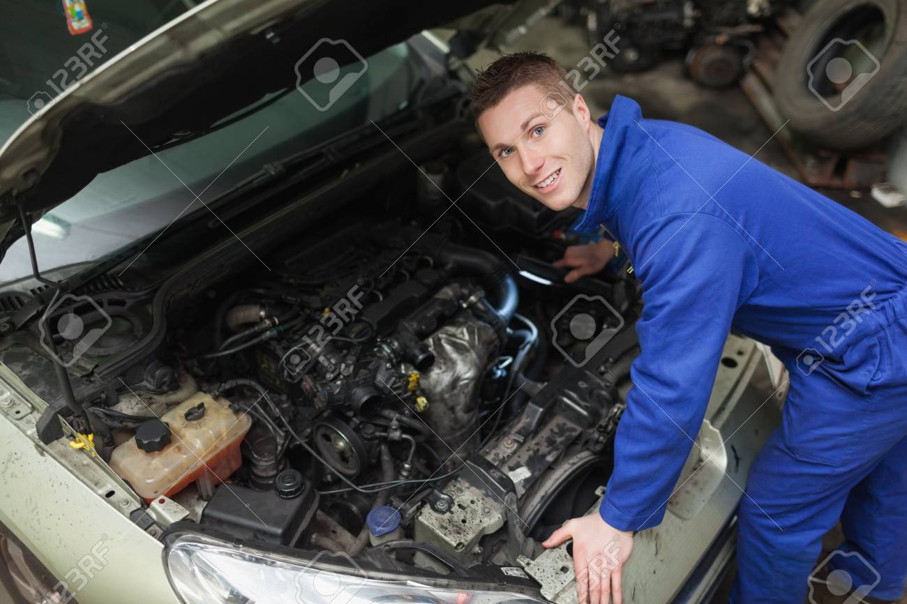 portrait of male mechanic with flashlight examining car engine stock
