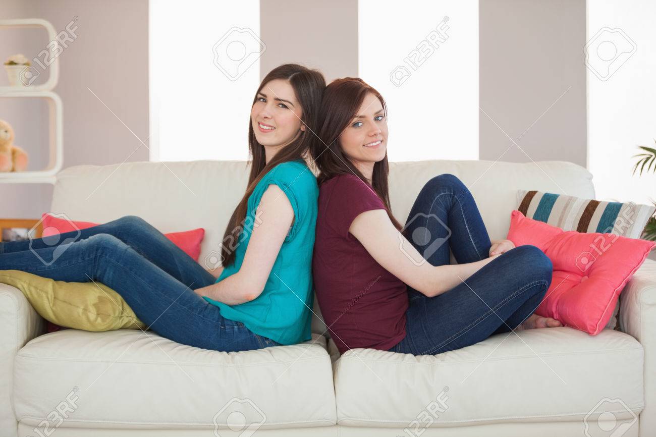 自宅のリビング ルームでソファの上に背中合わせに座っている笑顔の 2 人の友人 の写真素材 画像素材 Image 26740602