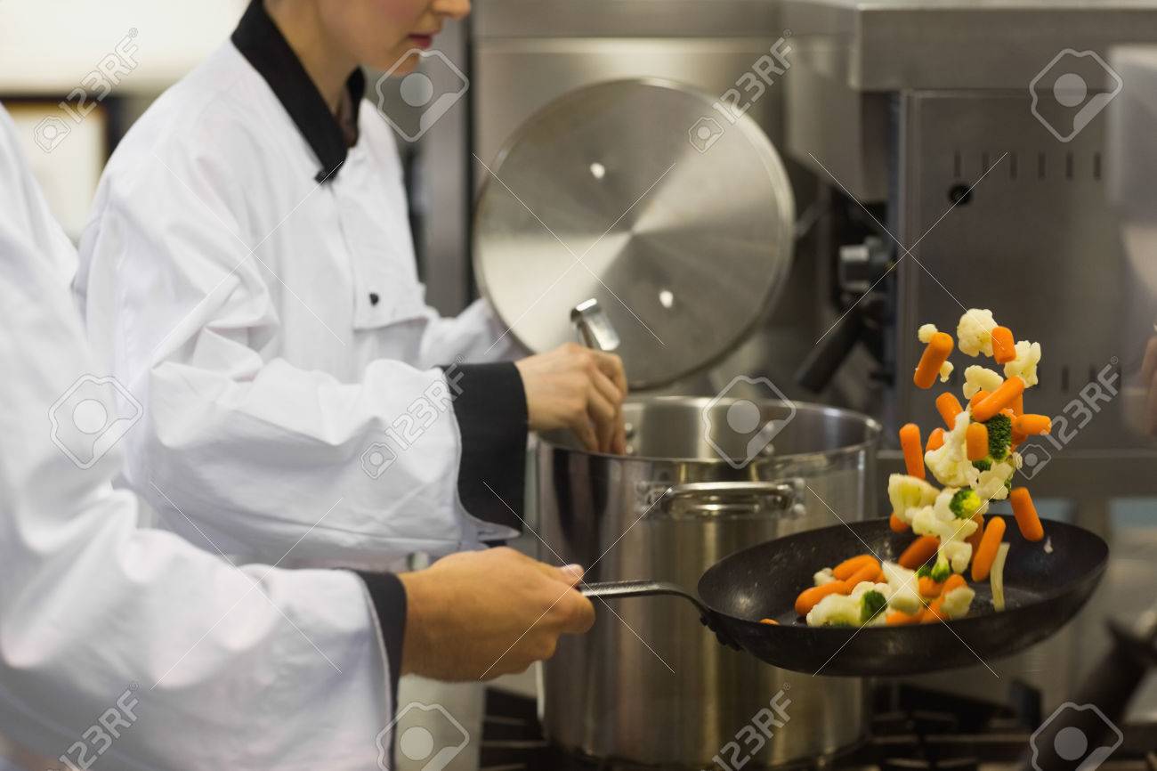 Busy Kitchen two chefs working in a busy kitchen at the stove one tossing Busy Kitchen two chefs working in a busy kitchen at the stove one tossing