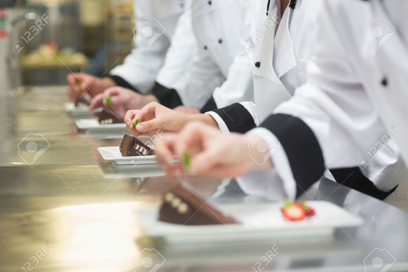 Busy Kitchen team of chefs garnishing dessert plates in a busy kitchen stock Busy Kitchen team of chefs garnishing dessert plates in a busy kitchen stock