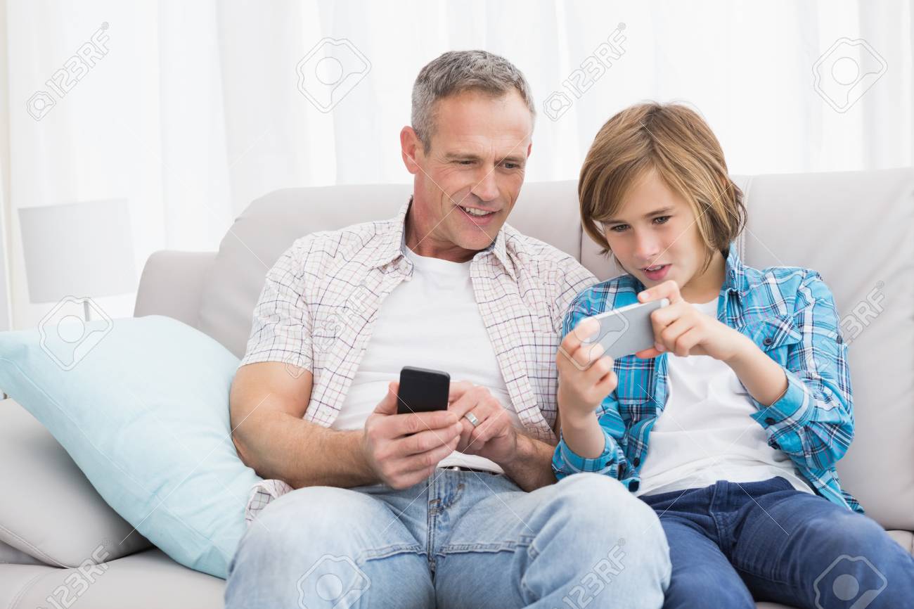 Son Showing Something On His Mobile Phone To His Father At Home In The  Living Room Stock Photo, Picture And Royalty Free Image. Image 31892808.