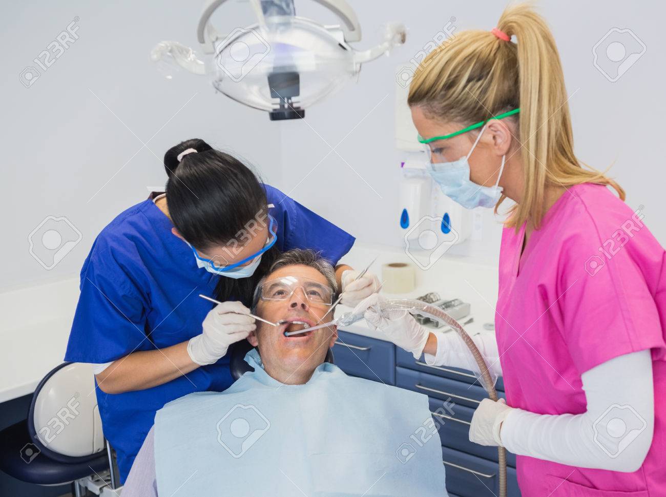 dentist examining a patient with her dental nurse holding suction dentel nurse