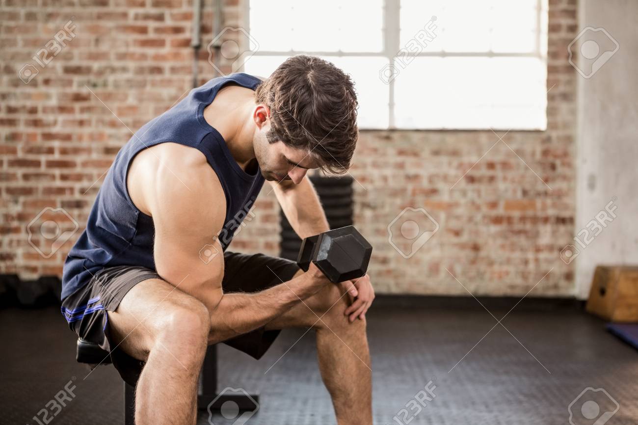 ジムで座りながら持ち上げるダンベルを男します の写真素材 画像素材 Image
