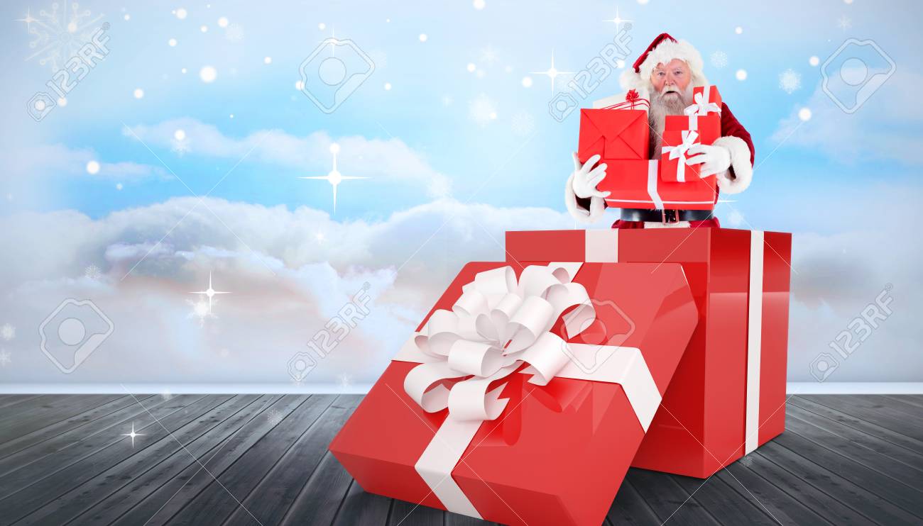 santa standing in large gift against clouds in a room stock photo
