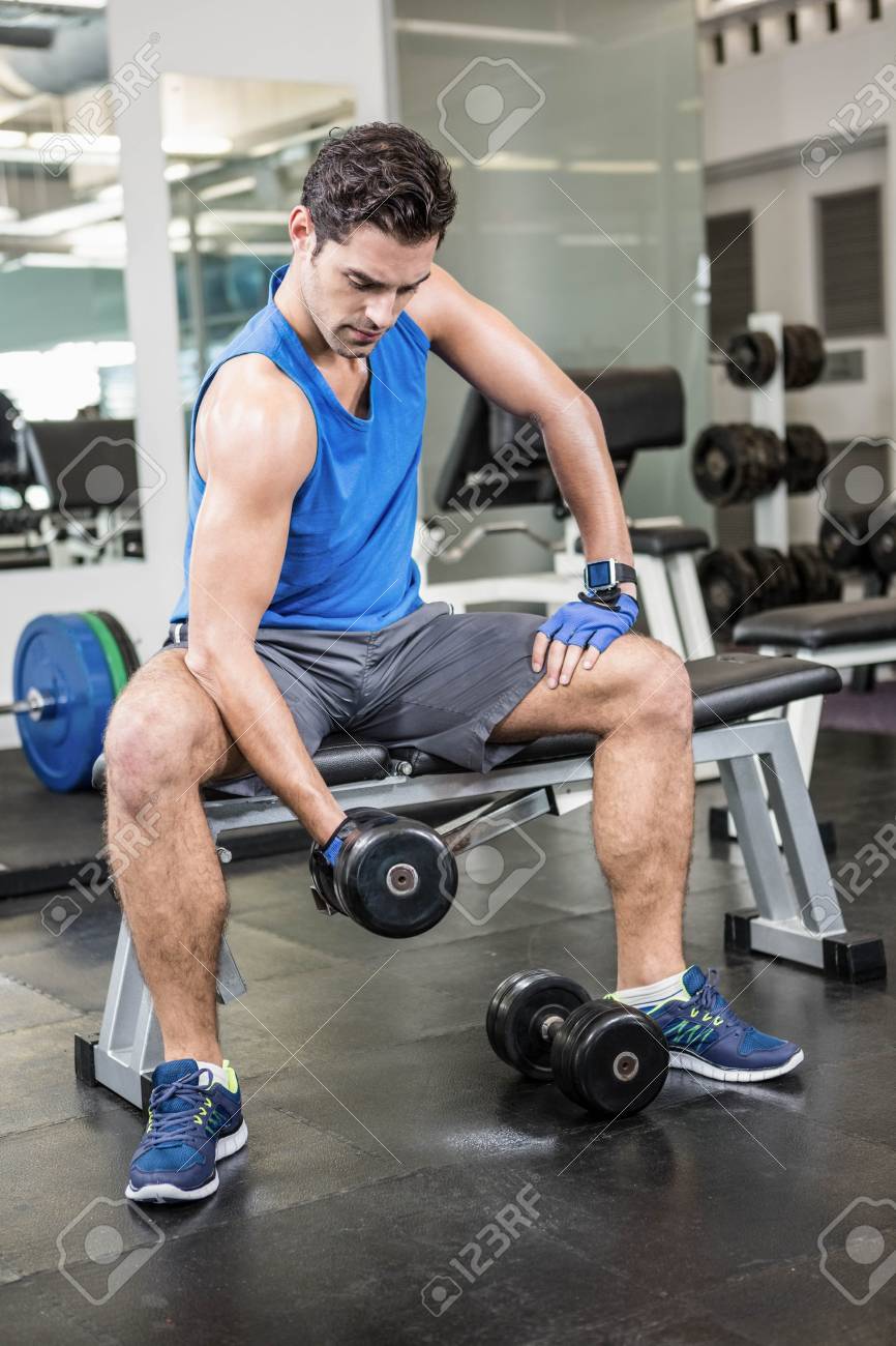 ジムでベンチに座りながらダンベルを持ち上げる筋肉の男 の写真素材 画像素材 Image