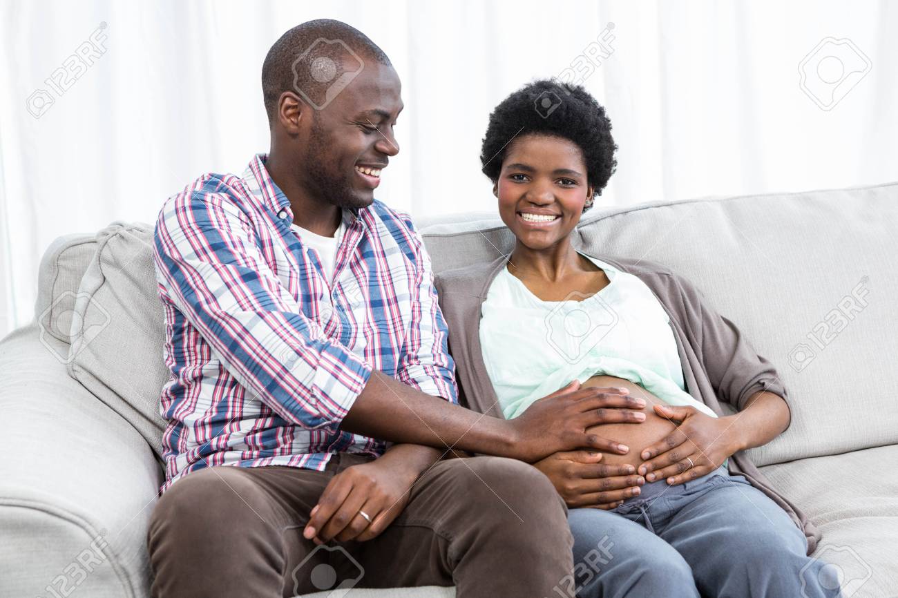 自宅のソファの上の妊娠中の梨花の胃に触れる男の肖像 の写真素材 画像素材 Image