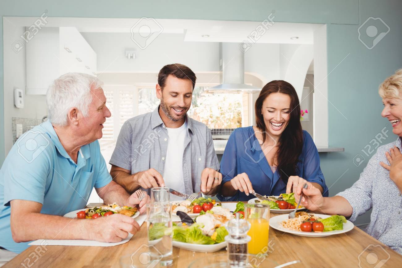Family laughing while sitting at dining table with food in home - 53891906 Importantcool.com