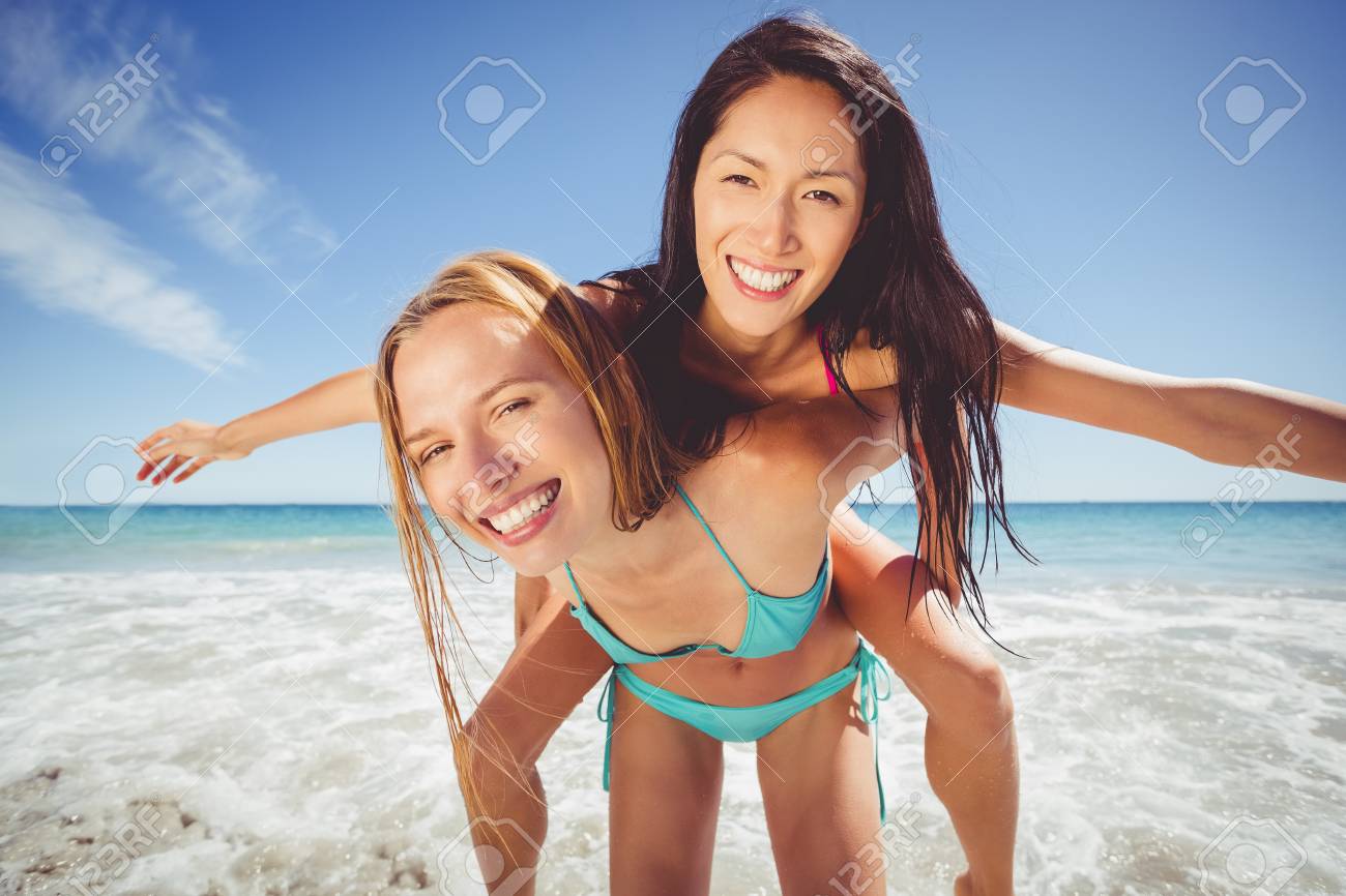 若い女性与える貯金箱の肖像画はビーチで彼女の女友達に戻る の写真素材 画像素材 Image 57121764
