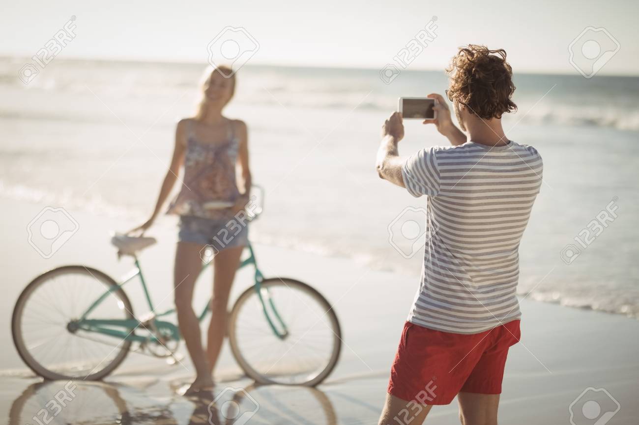 Bemannen Sie Das Fotografieren Der Frau Die Fahrrad Auf Ufer Am Strand Wahrend Des Sonnigen es Bereitsteht Lizenzfreie Fotos Bilder Und Stock Fotografie Image