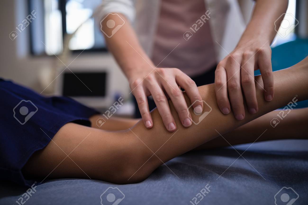 Midsection of female therapist massaging calf with boy lying on bed at hospital ward - 82492656 Midsection of female therapist massaging calf with boy lying on bed at hospital ward - 82492656