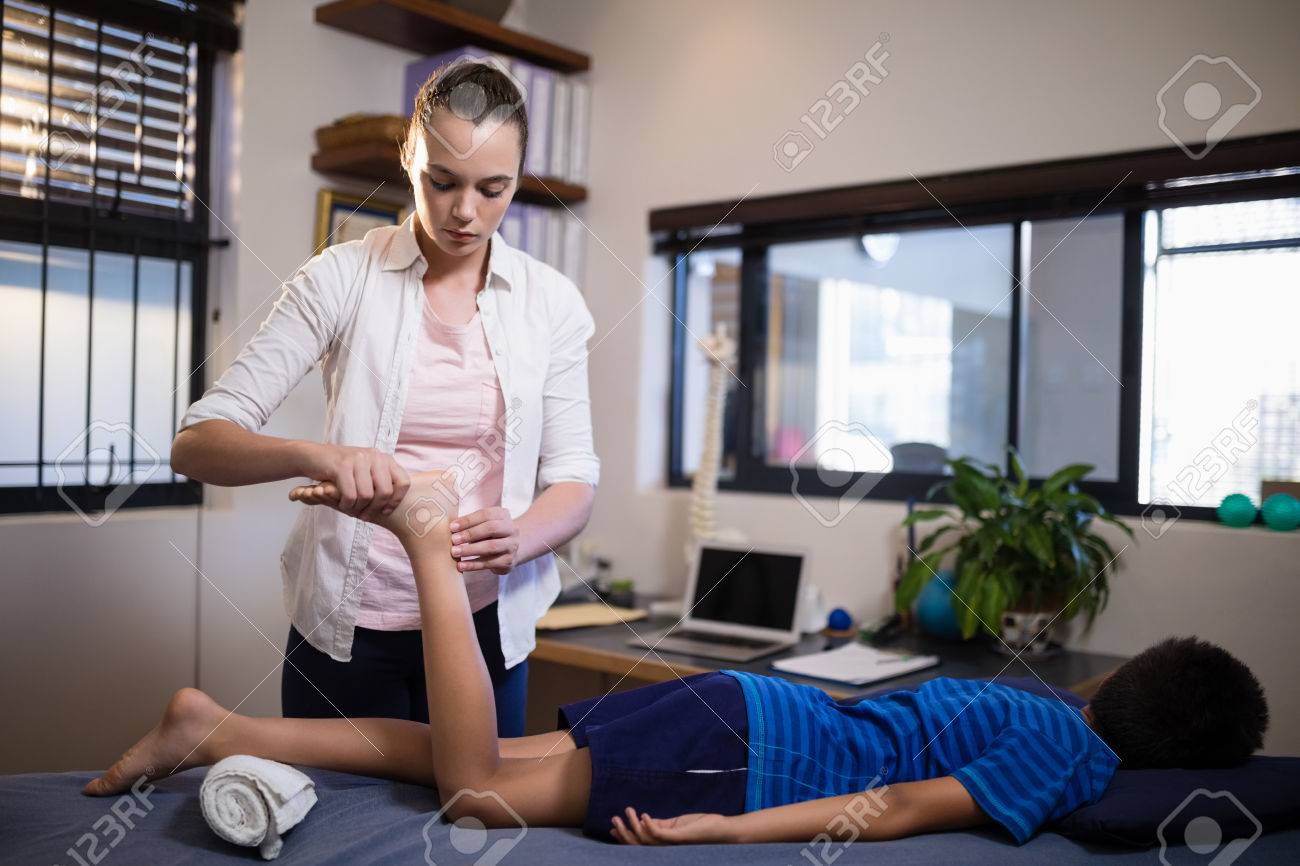 病棟のベッドで横たわっている少年ながら足の裏をマッサージの若い女性セラピスト の写真素材 画像素材 Image