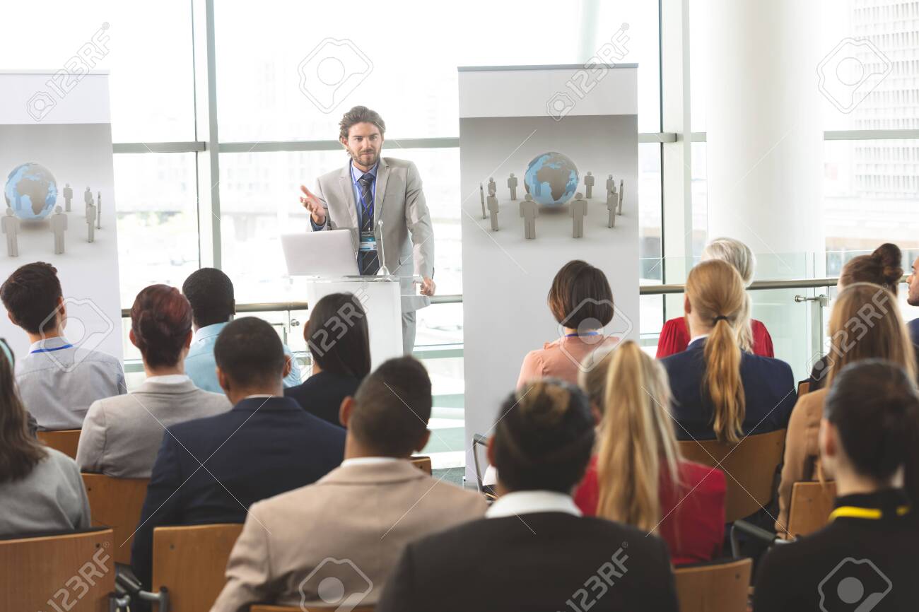 Front view of Caucasian businessman with laptop speaks in front of diverse crowd of business people at business seminar in office building - 121810991 Front view of Caucasian businessman with laptop speaks in front of diverse crowd of business people at business seminar in office building - 121810991