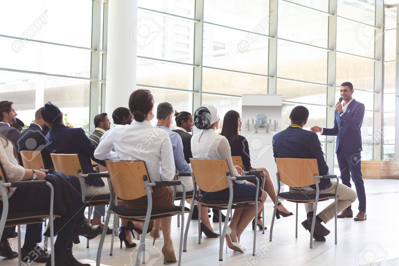 Front view of handsome mixed-race businessman speaking at business seminar with diverse business people listening to him at conference - 122224022 Front view of handsome mixed-race businessman speaking at business seminar with diverse business people listening to him at conference - 122224022