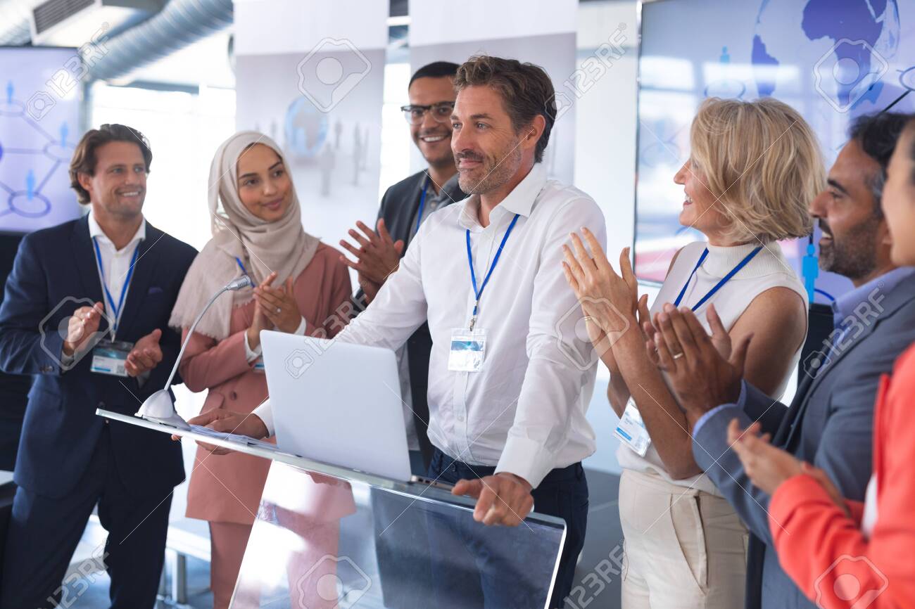 Front view of mature Caucasian businessman standing with diverse colleagues and speaks in a business seminar. International diverse corporate business partnership concept - 127165267 Front view of mature Caucasian businessman standing with diverse colleagues and speaks in a business seminar. International diverse corporate business partnership concept - 127165267