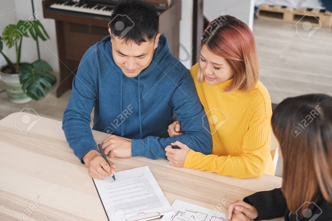 Asian happy couple sign contract buying new home with realtor agent with smiling face at new home.buying new house real estate - 112241516 Asian happy couple sign contract buying new home with realtor agent with smiling face at new home.buying new house real estate - 112241516