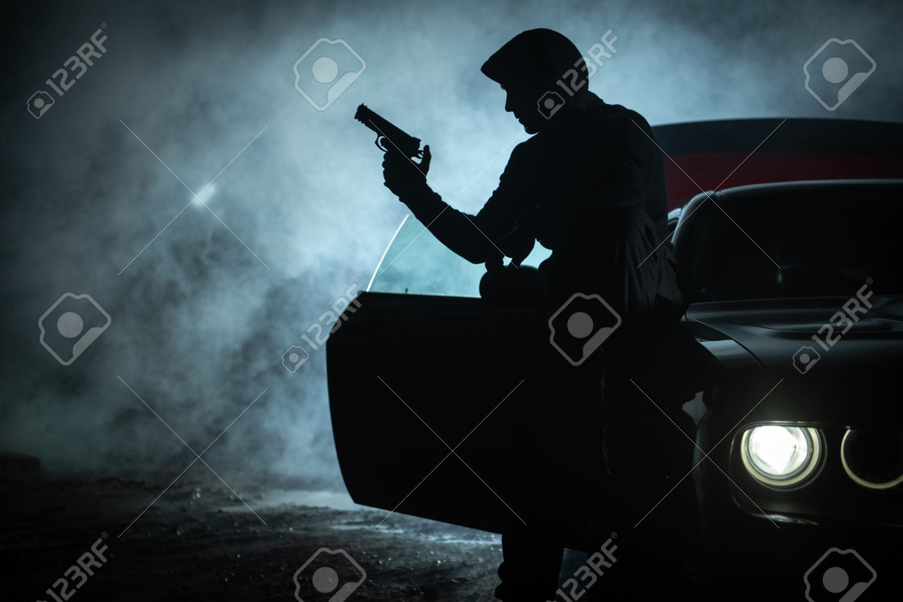 Caucasian Pensive Gangster in His 40s Playing with His Handgun During Late Night. Seating on His Car Hood. Drama and Darkness. Outlaw Theme. - 169664981 Caucasian Pensive Gangster in His 40s Playing with His Handgun During Late Night. Seating on His Car Hood. Drama and Darkness. Outlaw Theme. - 169664981
