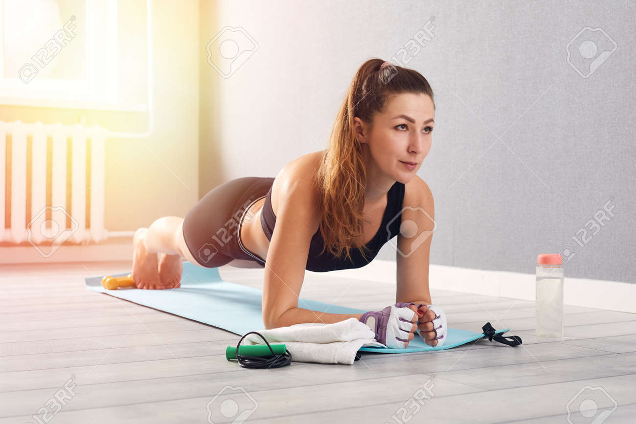 Woman In Fitness Wear Doing Exercise At Home. Time for yoga. healthy girl doing exercises while resting at home. Fitness, relaxation, stay home concept - 169825934 Woman In Fitness Wear Doing Exercise At Home. Time for yoga. healthy girl doing exercises while resting at home. Fitness, relaxation, stay home concept - 169825934