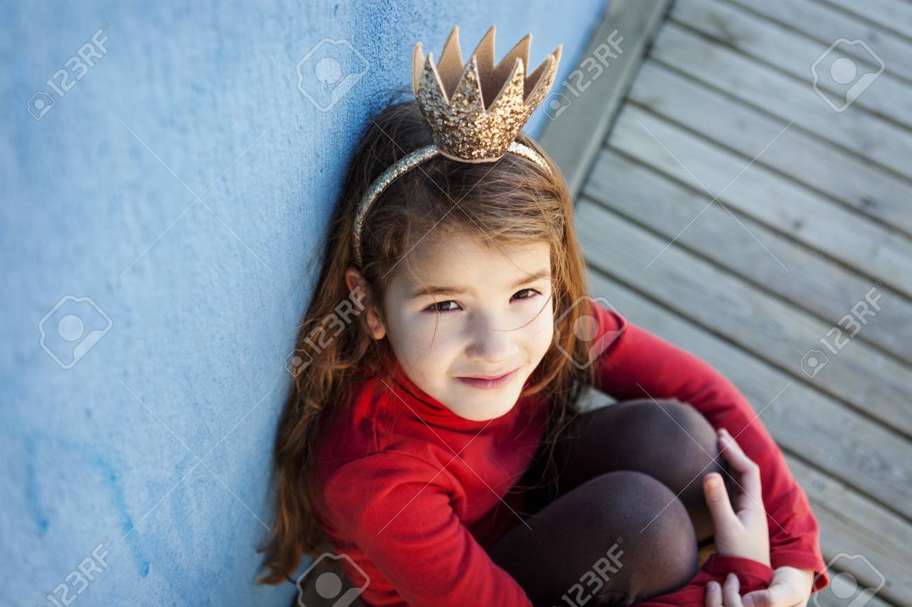Portrait Of Little Girl With A Crown Leaning Against Blue Wall