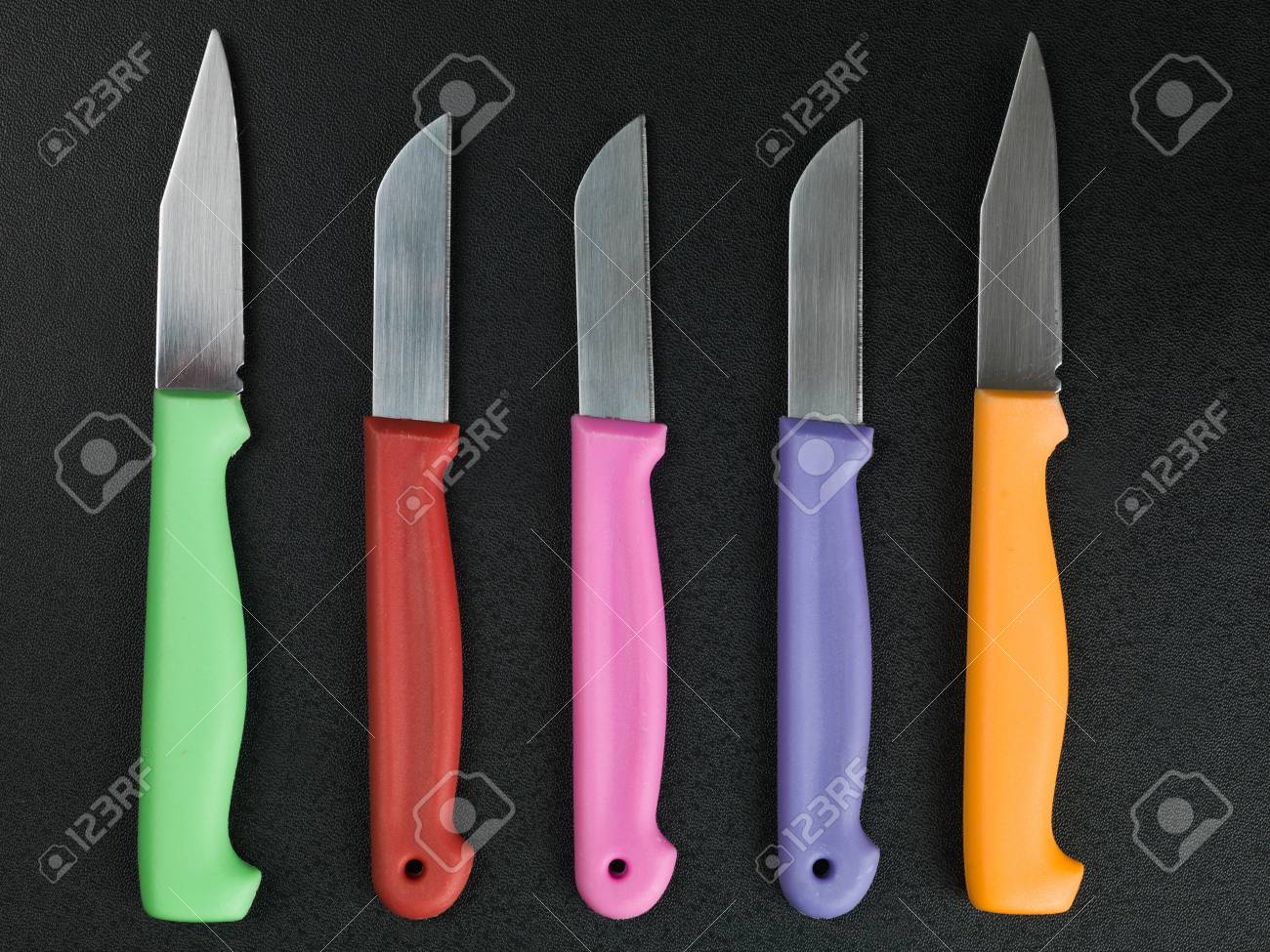 Set Of Colorful Kitchen Knives Against A Black Background Stock