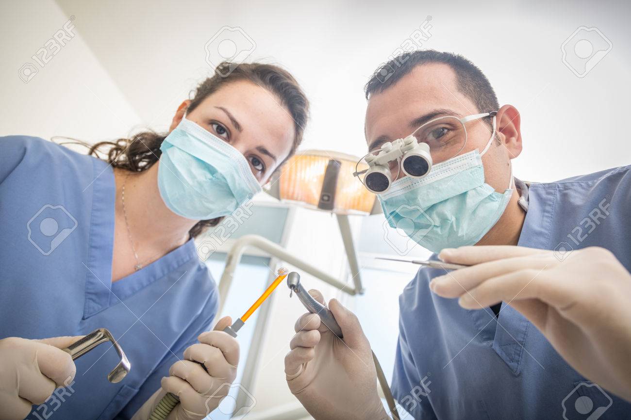 陽気な歯科カメラ目線歯科用ツールを保持しています 個人情報や患者の視点 ハメ撮り 彼らは ドリル ミラー 吸引器 スプレッダーを保持しています 歯科医は 歯科用ルーペを着ています の写真素材 画像素材 Image