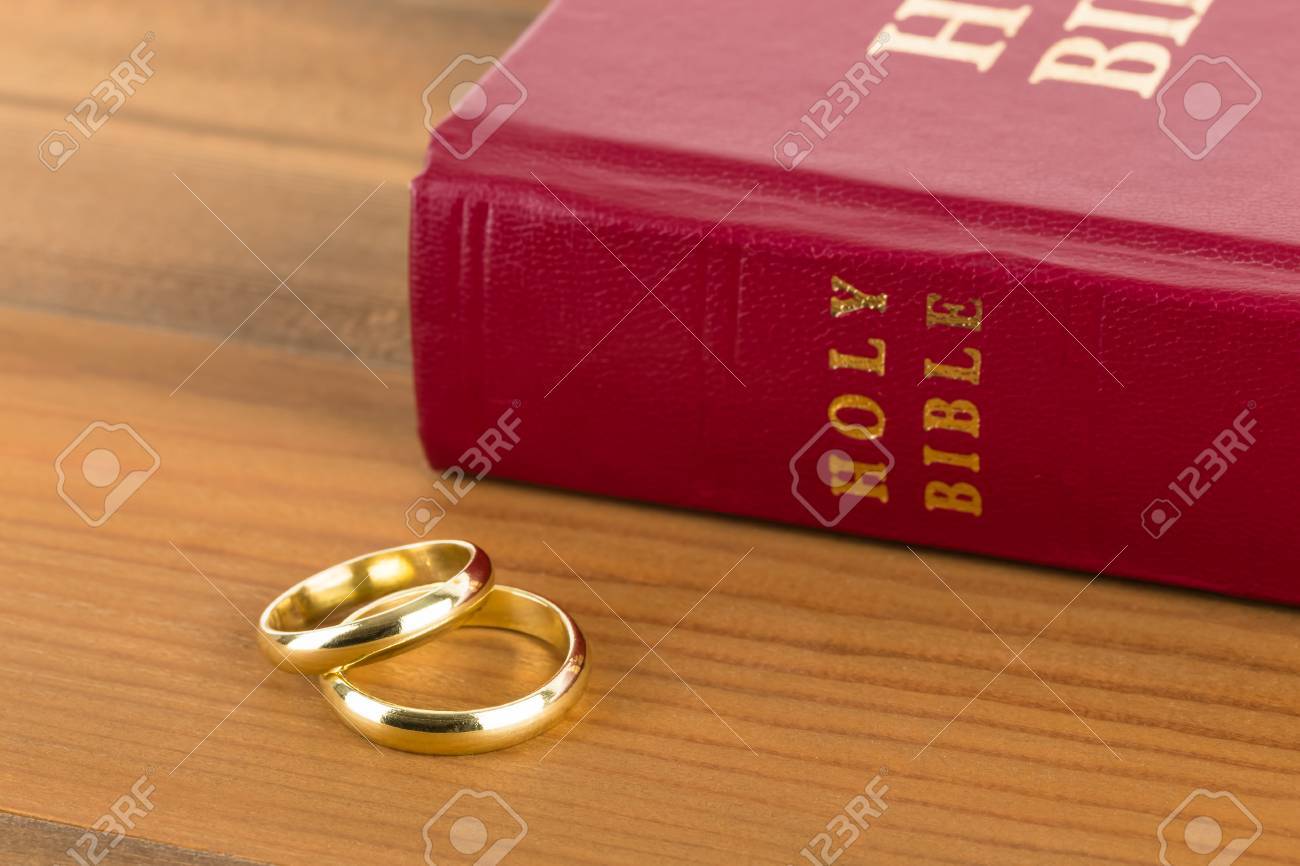 gold wedding rings on wooden table and red bible book stock photo