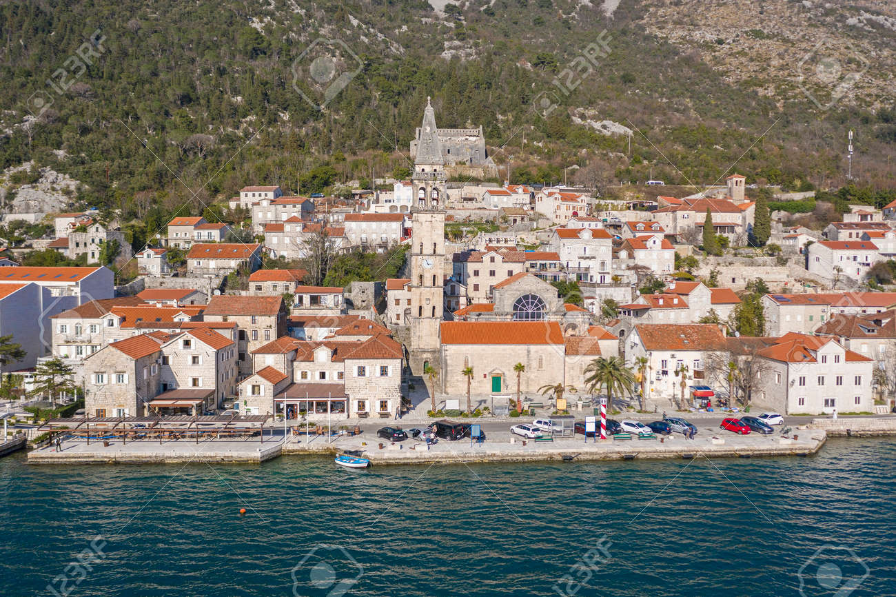 Aerial shot of the old coastal town of Perast at the foot of the mountain. Seaside promenade, residential buildings with traditional balkan red roofs, ancient Cathedral and coastline - 165655001 Aerial shot of the old coastal town of Perast at the foot of the mountain. Seaside promenade, residential buildings with traditional balkan red roofs, ancient Cathedral and coastline - 165655001