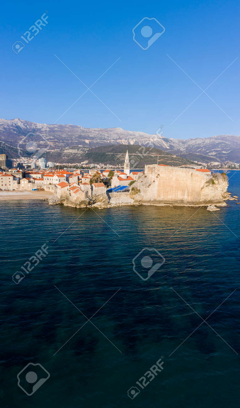 Aerial View of Budva Old Town and sandy beach in a beautiful spring day. Top view from drone on the old fortress and azure sea. Vertical panorama, Montenegro - 165655013 Aerial View of Budva Old Town and sandy beach in a beautiful spring day. Top view from drone on the old fortress and azure sea. Vertical panorama, Montenegro - 165655013