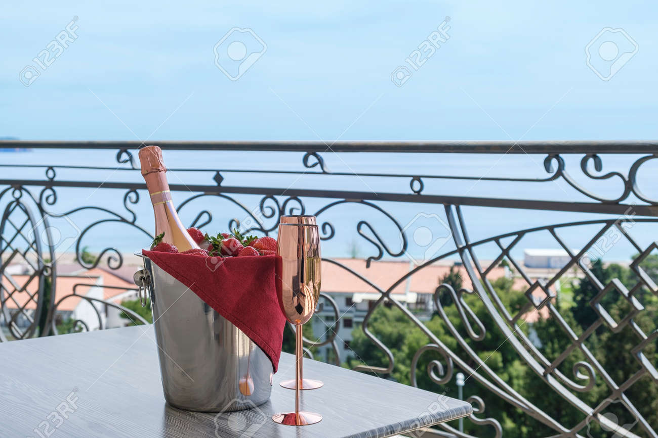 Served table on the terrace of a luxury villa with sea view. On the table are a bucket with champagne, strawberries and two empty glasses. Through the balcony lattice we see the blue sky and the azure sea - 170377753 Served table on the terrace of a luxury villa with sea view. On the table are a bucket with champagne, strawberries and two empty glasses. Through the balcony lattice we see the blue sky and the azure sea - 170377753