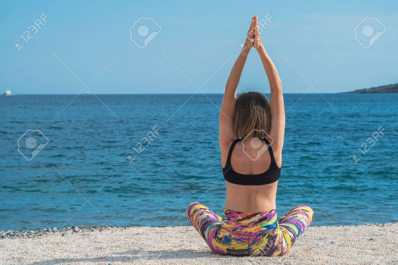 Young slim beautiful woman practicing yoga on the seashore, on the beach, against the background of the sea. Exercising, making yoga pose on the sandy beach. Back view - 171535645 Young slim beautiful woman practicing yoga on the seashore, on the beach, against the background of the sea. Exercising, making yoga pose on the sandy beach. Back view - 171535645