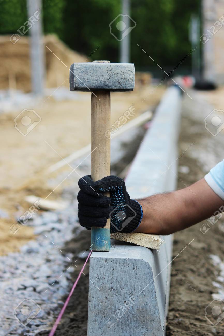 ワーカーのメイソンは バス用駐車場の工事中 歩道の縁石を置いたハンマーを示しています の写真素材 画像素材 Image
