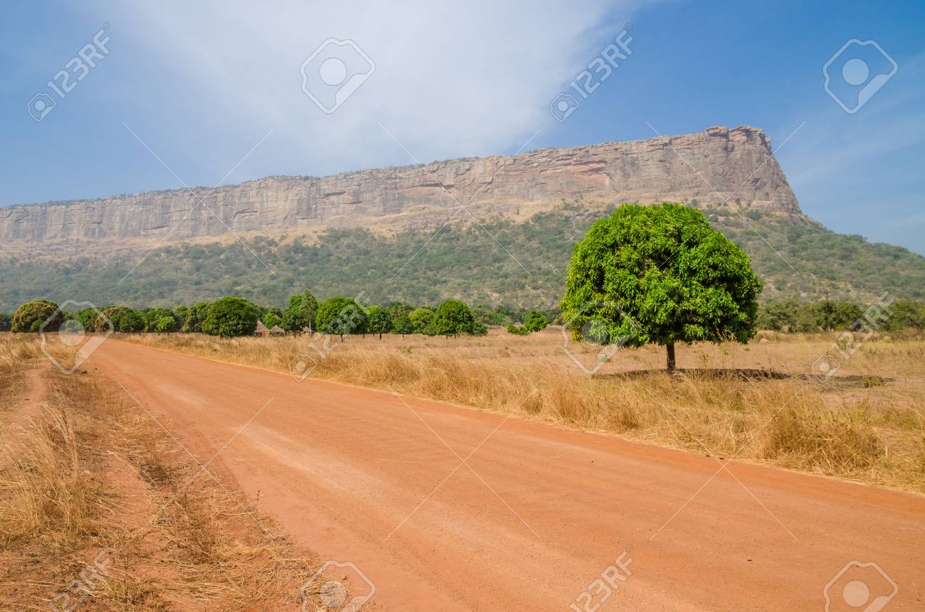Red dirt and gravel road, single trees and large flat topped mountain in Fouta Djalon region, Guinea, West Africa - 87602803 Red dirt and gravel road, single trees and large flat topped mountain in Fouta Djalon region, Guinea, West Africa - 87602803