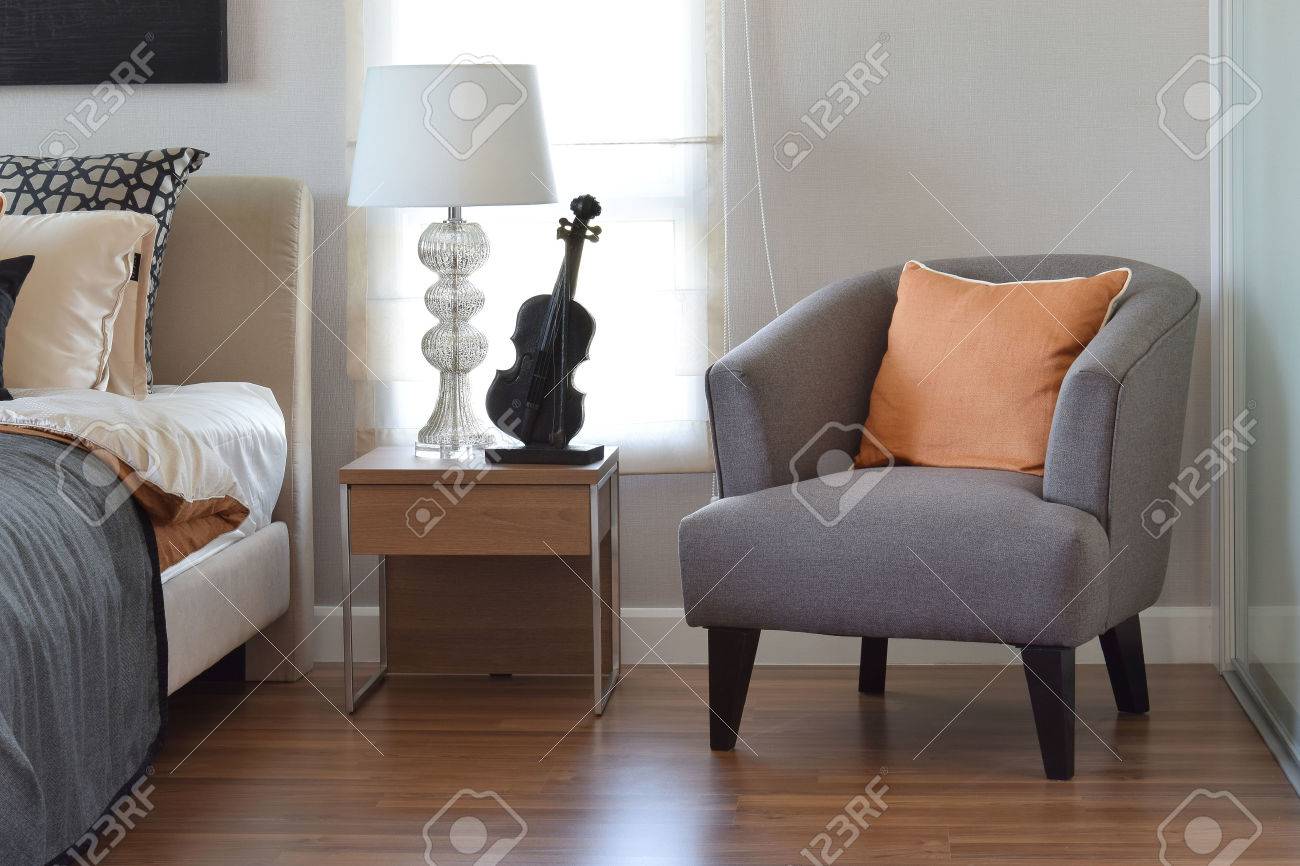 stock photo modern bedroom interior with orange pillow on grey chair and bedside table lamp at home - Chair As Bedside Table stock photo modern bedroom interior with orange pillow on grey chair and bedside table lamp at home - Chair As Bedside Table