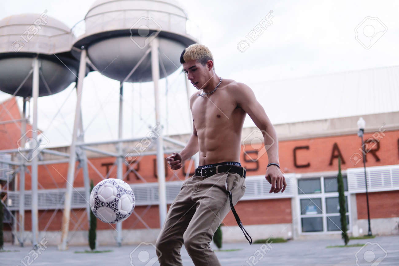 염색한 머리에 윗옷을 벗은 라틴계 소년이 도시 광장에서 축구를 하고 있다. 거리에서 축구 훈련을 하는 라틴계 남자. 도시 스타일의 검은  피부 소년이 공을 차고 있다. 고화질 사진 로열티 무료 사진, 그림, 이미지