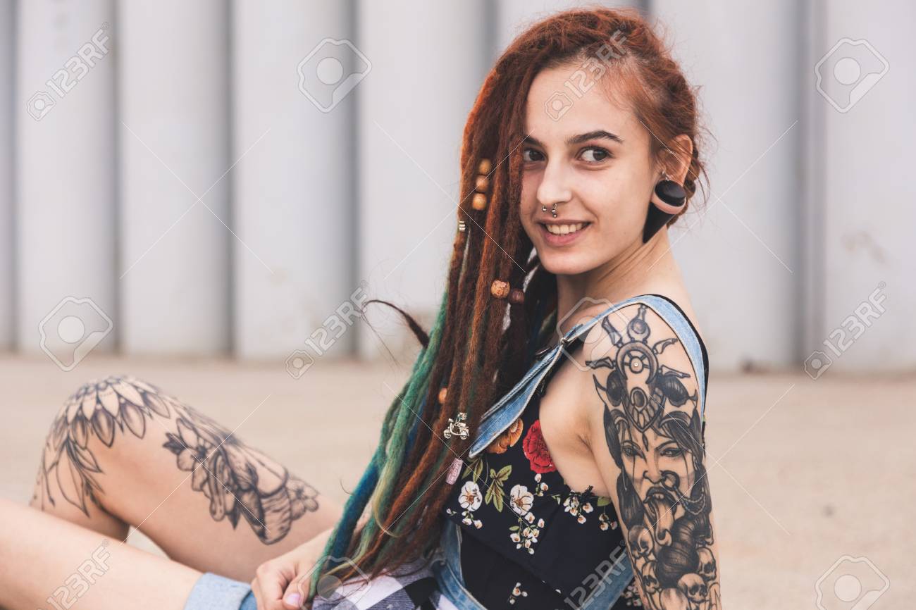 Young Girl With Tattoo And Dreadlocks Is Sitting On The Background