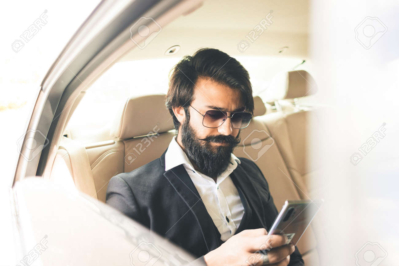 Stylish handsome Hindu businessman works in the backseat of the car and uses the phone. Safe and comfortable luxury travel - 171704367 Stylish handsome Hindu businessman works in the backseat of the car and uses the phone. Safe and comfortable luxury travel - 171704367