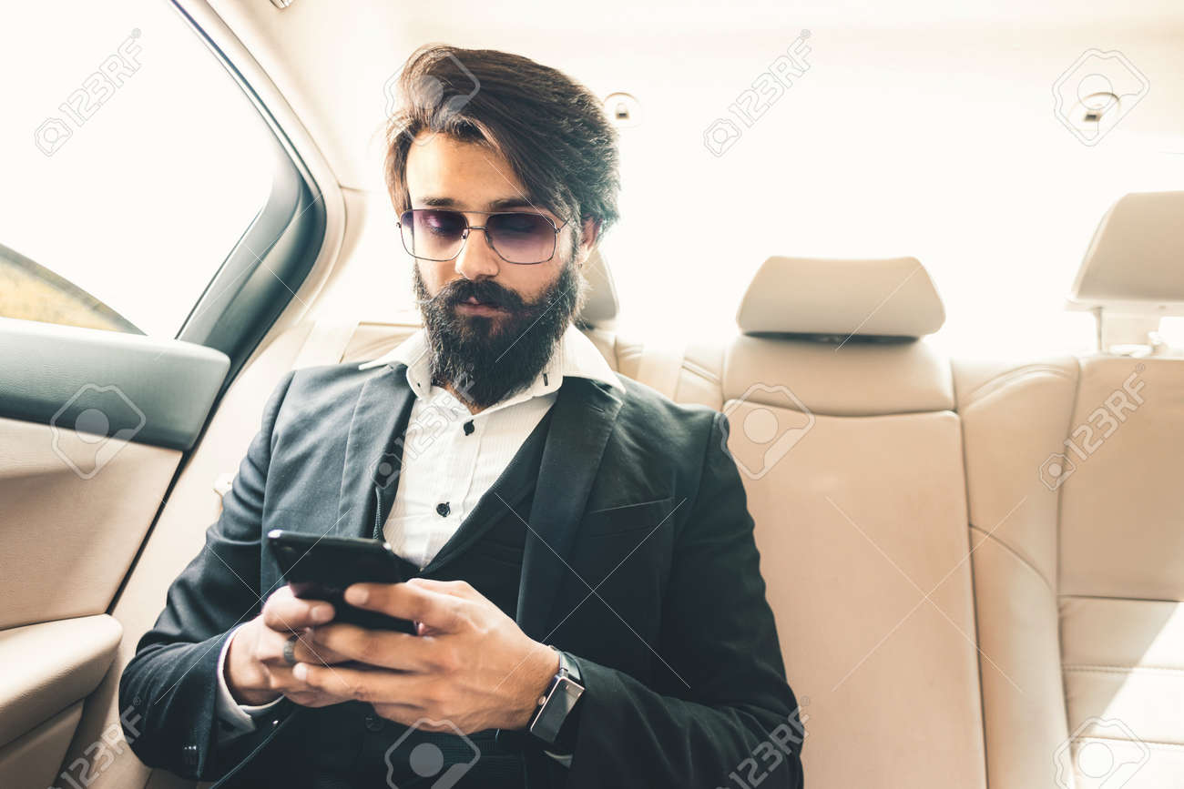 Stylish handsome Hindu boss with glasses and a beard works with the phone in the back seat of the car. Safe and comfortable business travel - 171617339 Stylish handsome Hindu boss with glasses and a beard works with the phone in the back seat of the car. Safe and comfortable business travel - 171617339