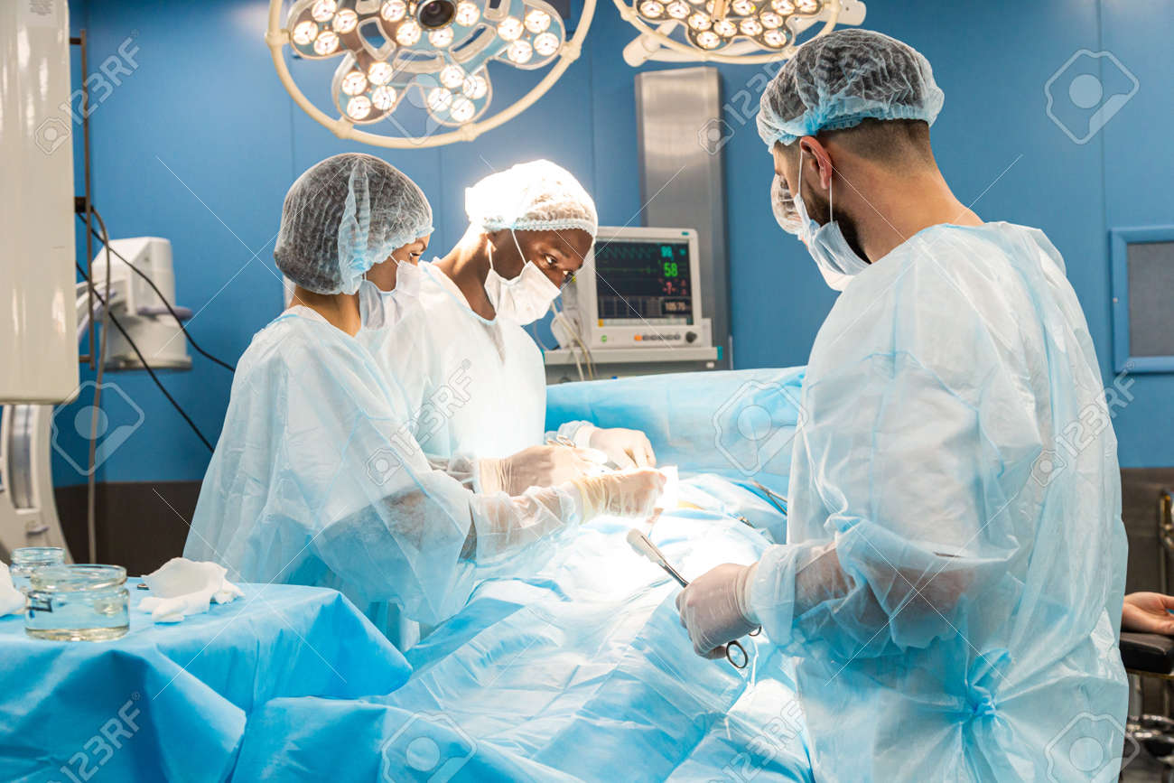 An international team of doctors performs a complex surgical operation on a patient under anesthesia. Modern operating room and experienced surgeons save lives - 171617363 An international team of doctors performs a complex surgical operation on a patient under anesthesia. Modern operating room and experienced surgeons save lives - 171617363
