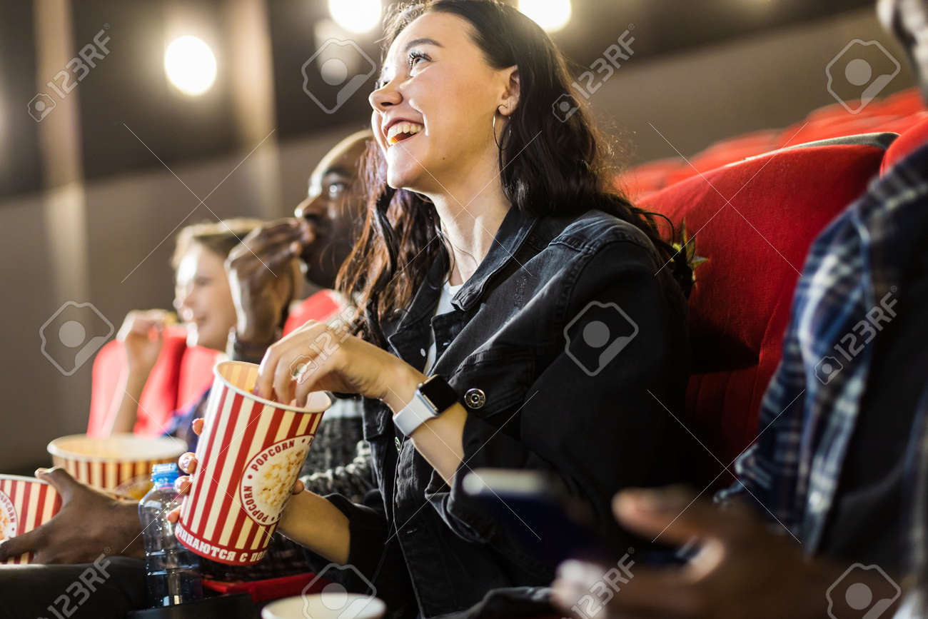 Friends are watching a movie in the cinema with popcorn. People sit in the armchairs of the cinema and look at the screen - 171660405 Friends are watching a movie in the cinema with popcorn. People sit in the armchairs of the cinema and look at the screen - 171660405