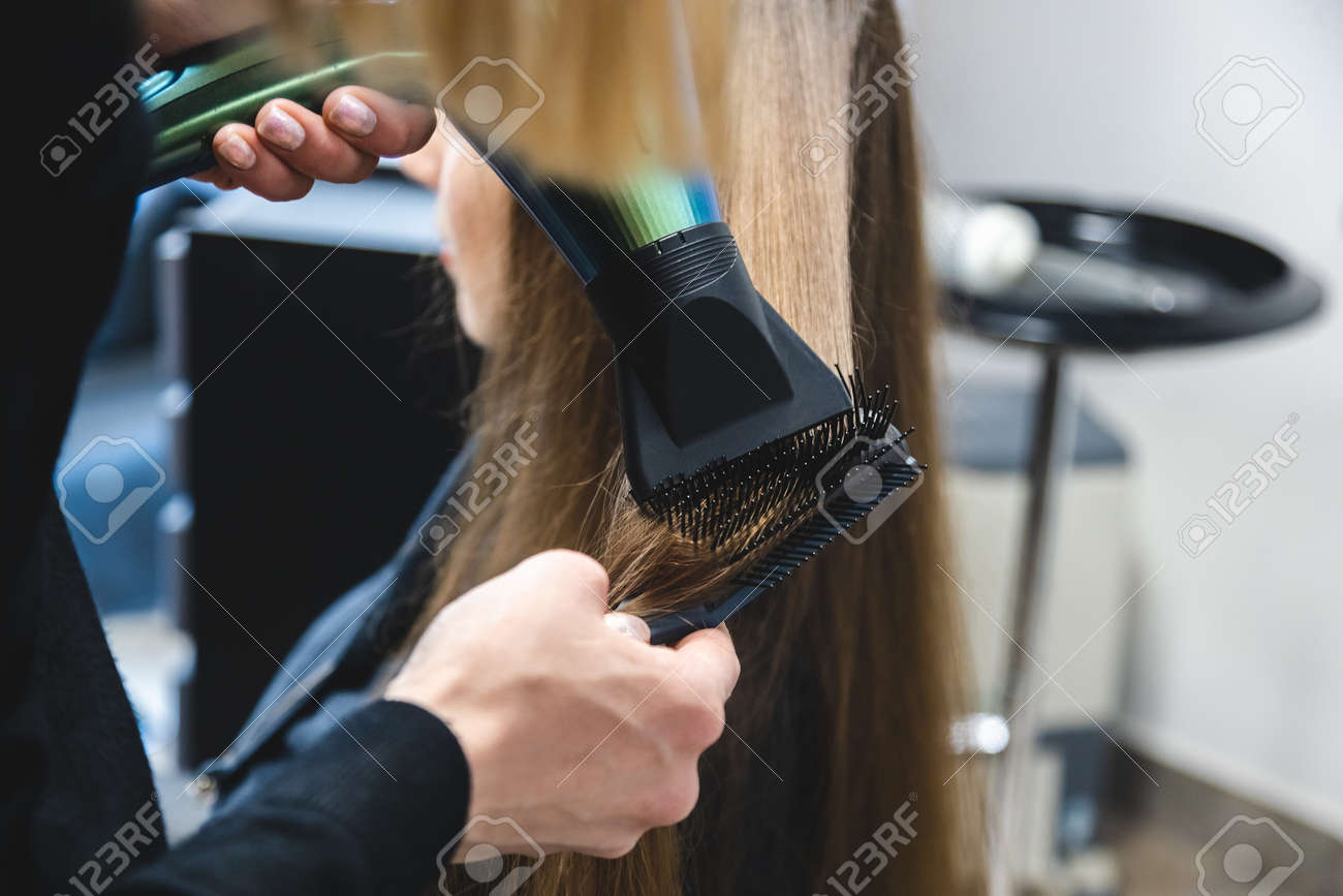 Cabeleireiro seca o cabelo com secador de cabelo para uma mulher