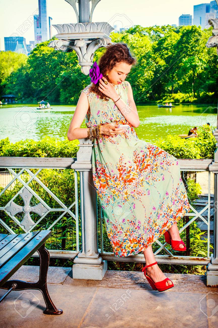 どこにでもテキスト メッセージ ノースリーブ ロングドレス 赤いサンダル靴のドレッシング 10 代の少女は座っているパビリオン スマート フォンを持っている手の中のメッセージを読みます 夏のファッション の写真素材 画像素材 Image