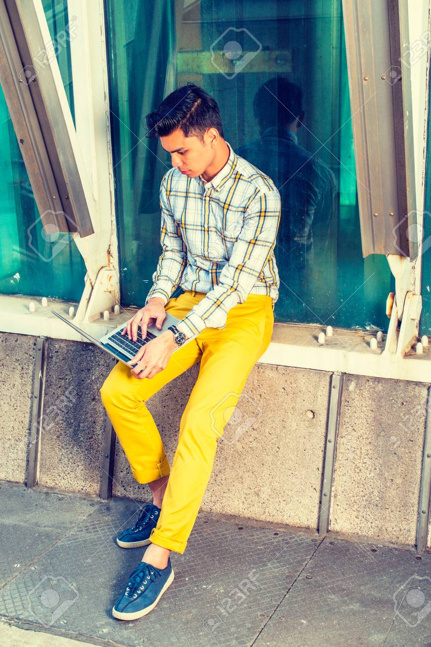 男は外で働きます 白 黄色柄シャツ 黄色のパンツ 青のスニーカーでドレッシング 若いハンサムな大学生は座っている金属構造体で ガラスの壁にラップトップ コンピューター上で作業します の写真素材 画像素材 Image 0393