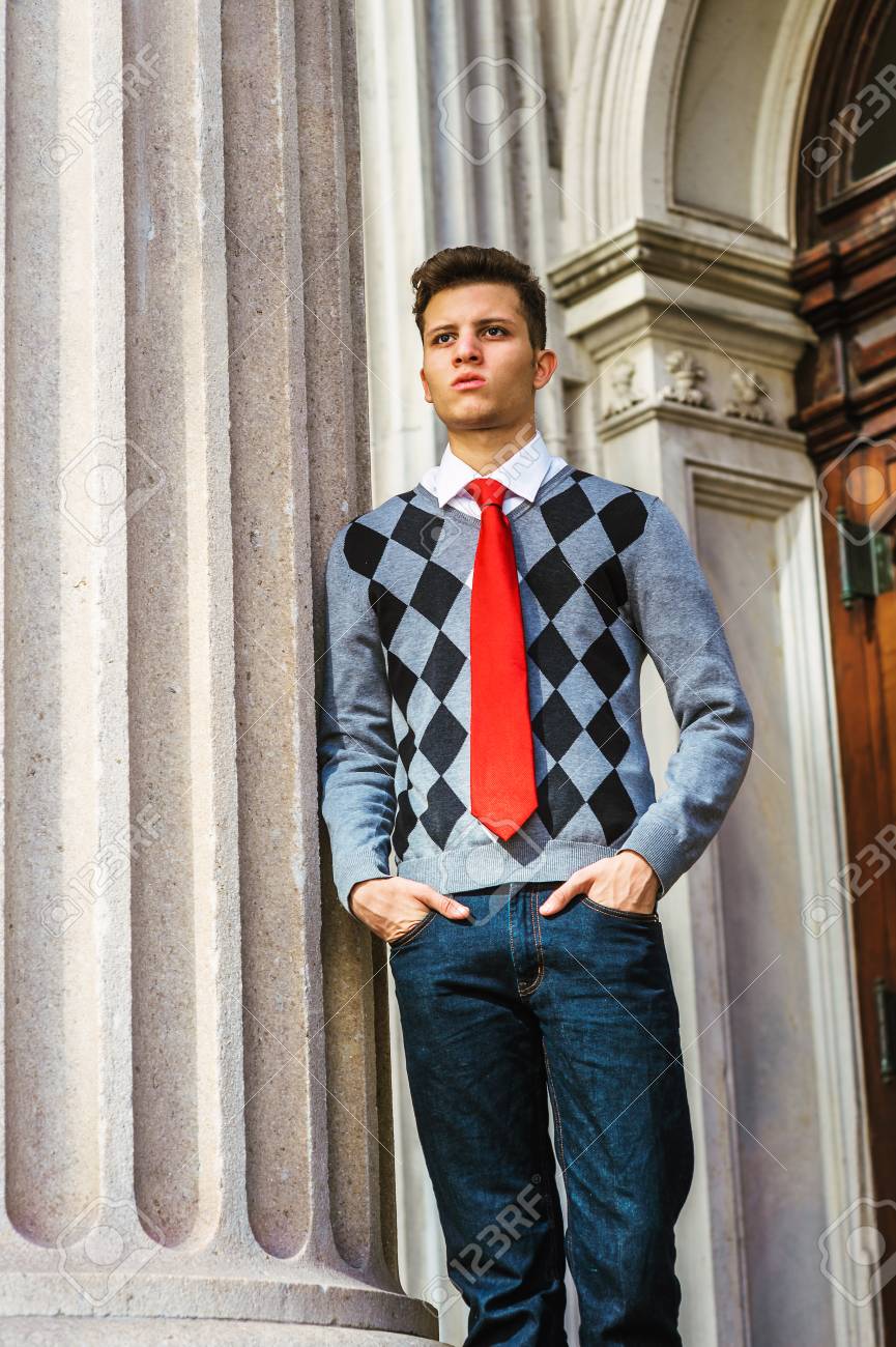ニューヨークに留学中のアメリカ人大学生 黒 白 灰色の模様のセーター 赤いネクタイ ジーンズ ヴィンテージスタイルのオフィスの外に立っている若い男を着て 考え 思考に迷った の写真素材 画像素材 Image