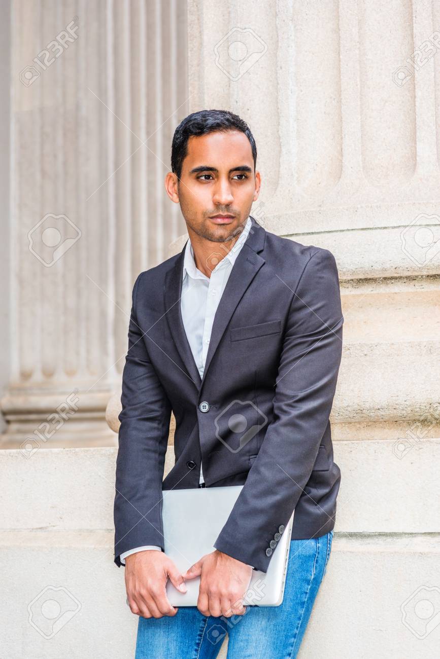 Young Hispanic American Businessman Working In New York Wearing Black Blazer White Shirt Blue Jeans Holding Laptop Computer Standing Against Column Of Old Office Doorway Looking Down Thinking Stock Photo Picture And