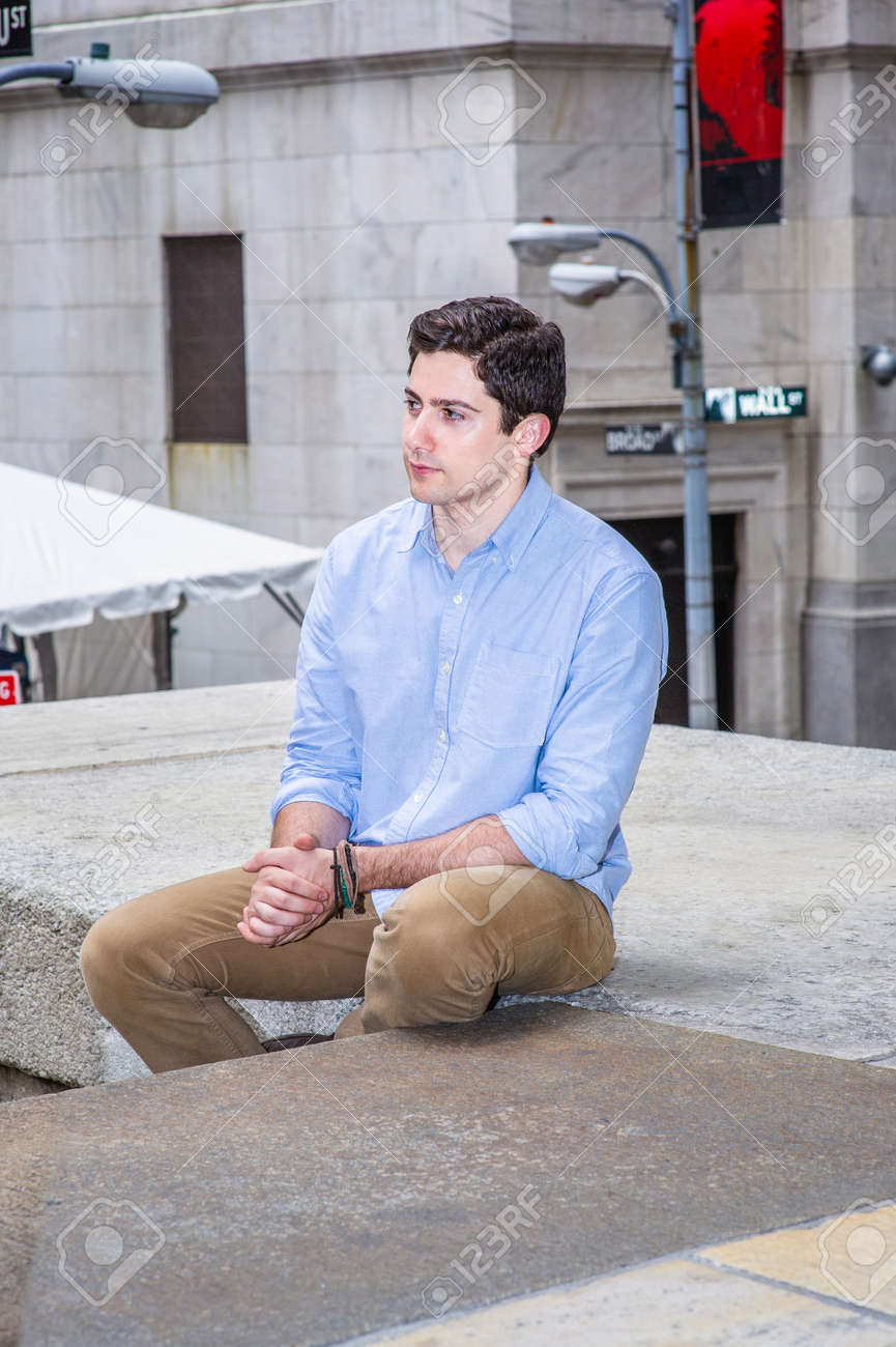 Clamping his hands and looking forward, a young handsome guy is sitting on a stage in the corner of the street, relaxing and thinking. - 171462631 Clamping his hands and looking forward, a young handsome guy is sitting on a stage in the corner of the street, relaxing and thinking. - 171462631