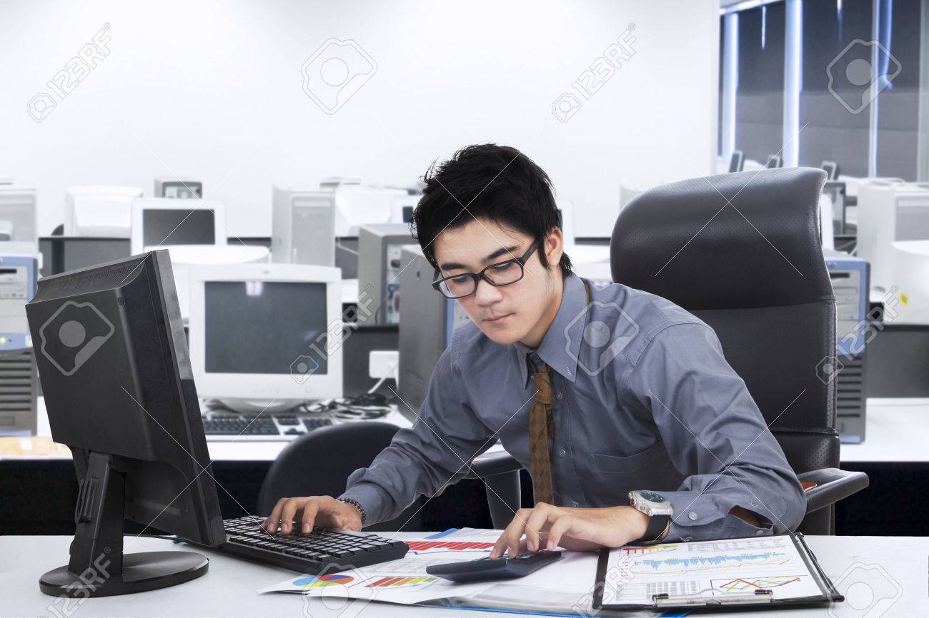 Male Entrepreneur Is Busy With His Work In The Office Using Computer And Calculator Stock Male Entrepreneur Is Busy With His Work In The Office Using Computer And Calculator Stock