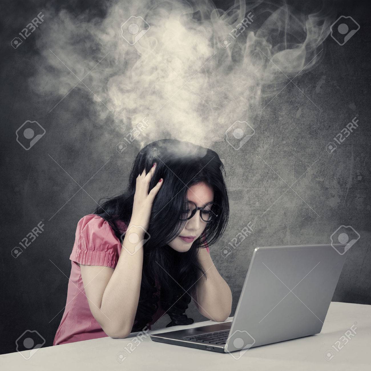 ノート パソコンで作業しながら彼女の頭から出てくる煙と緊張に満ちた若い実業家の画像 の写真素材 画像素材 Image