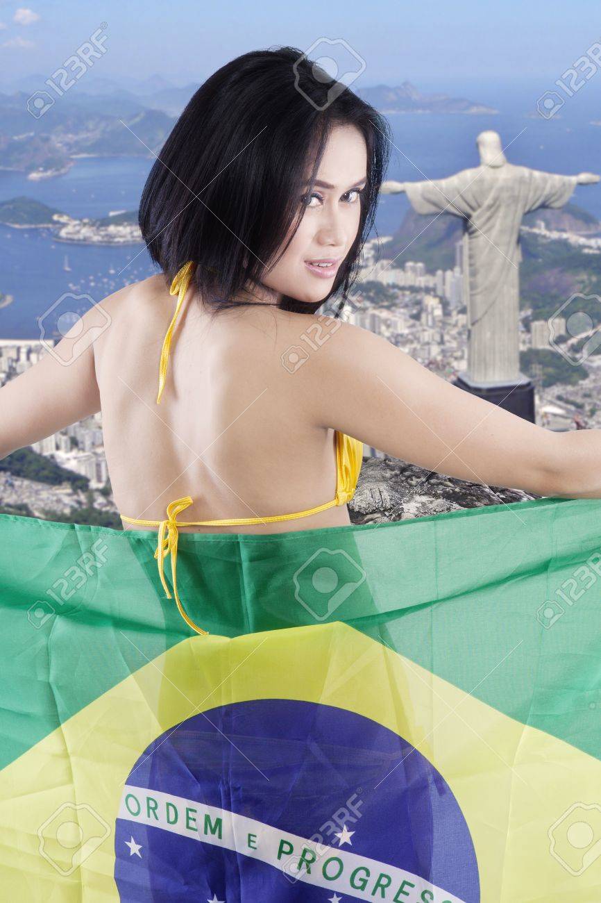 セクシーな女の子がブラジルのリオ デ ジャネイロ市背景を持つ旗を押しながらカメラで笑顔の裏側 の写真素材 画像素材 Image